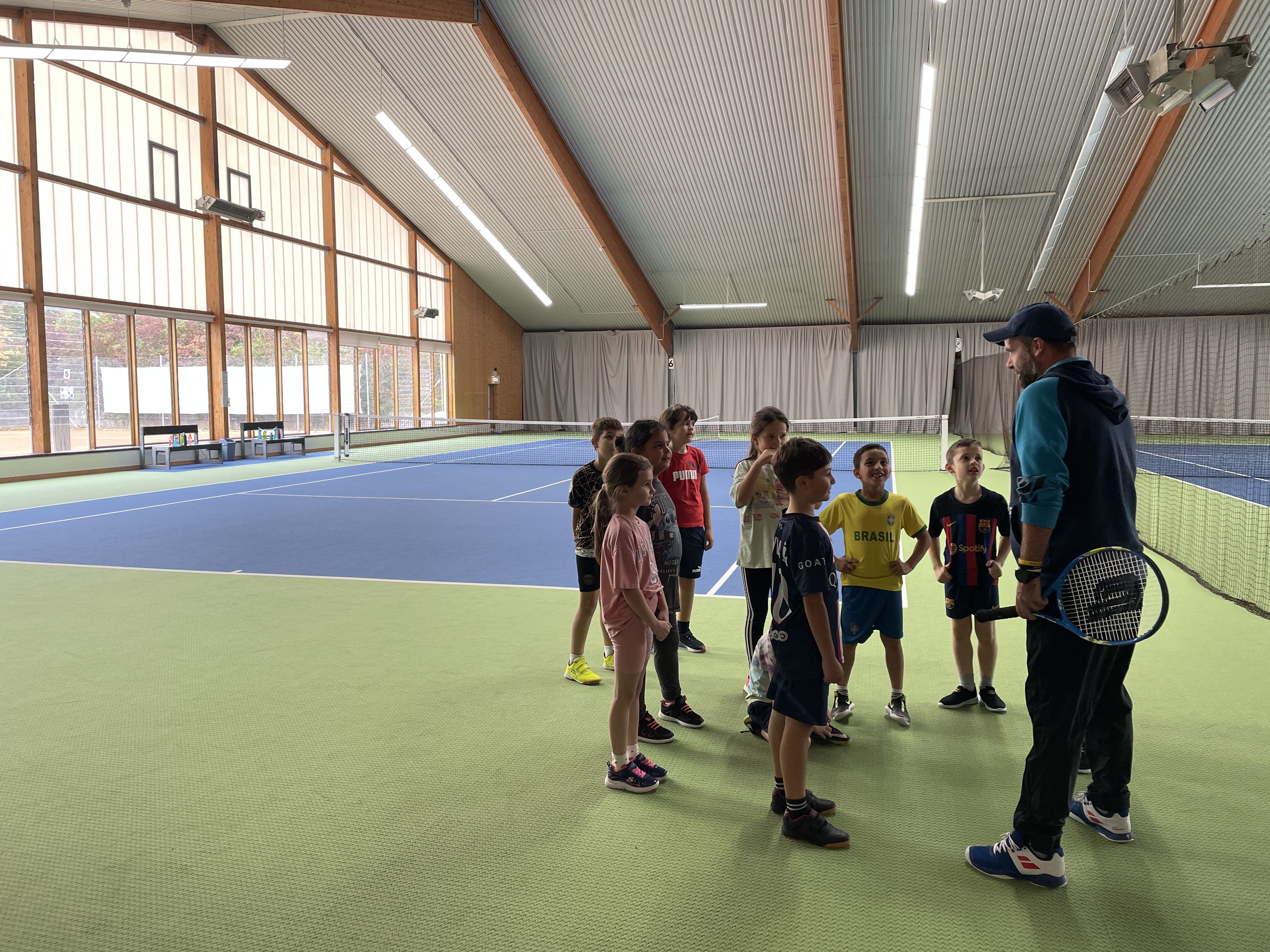 Bildbeschreibung: Kinder stehen sich an einem Tennisnetz gegenüber und spielen Tennis.