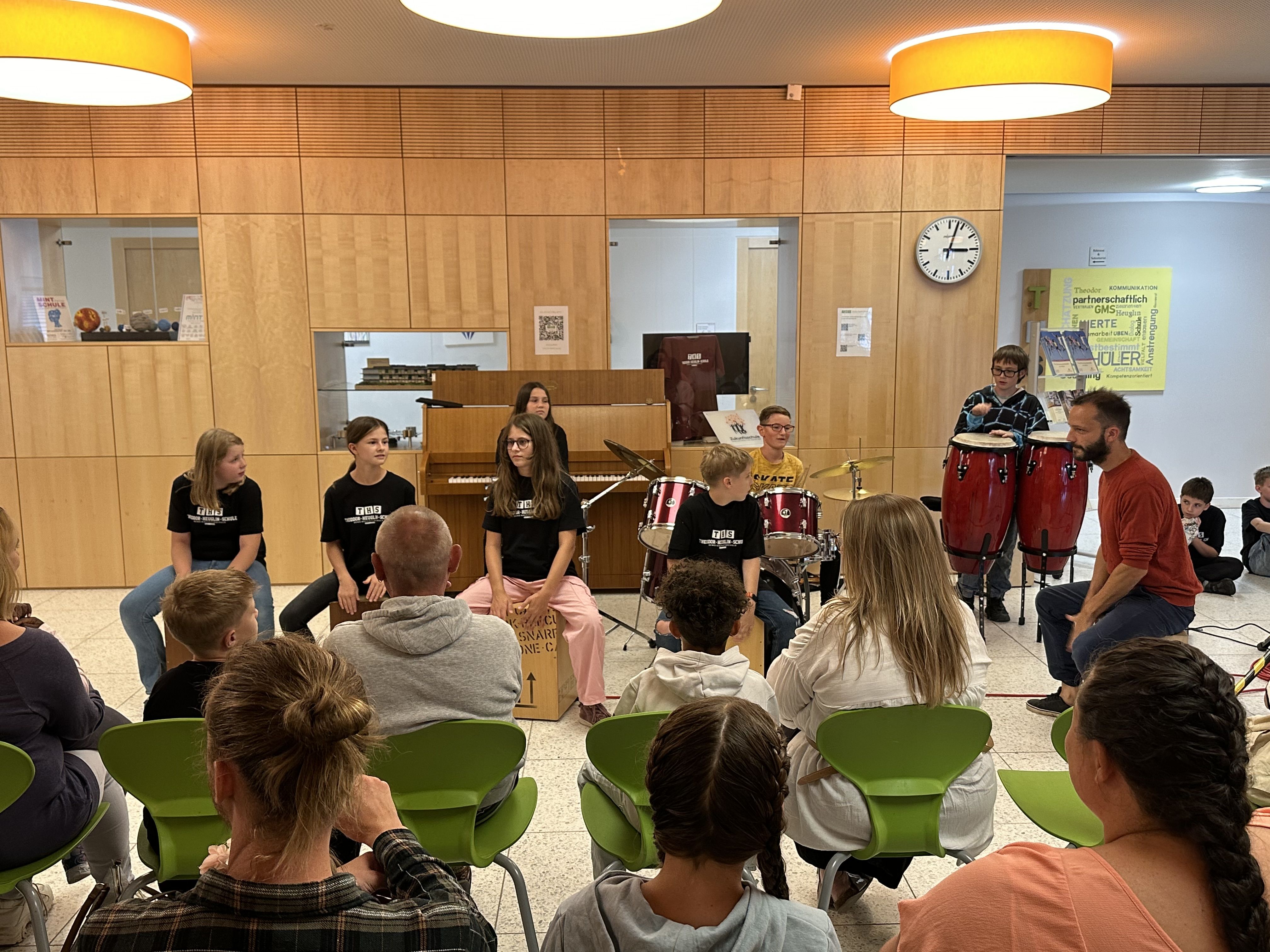 Eine Schülergruppe sitzt in der Aula und trommelt