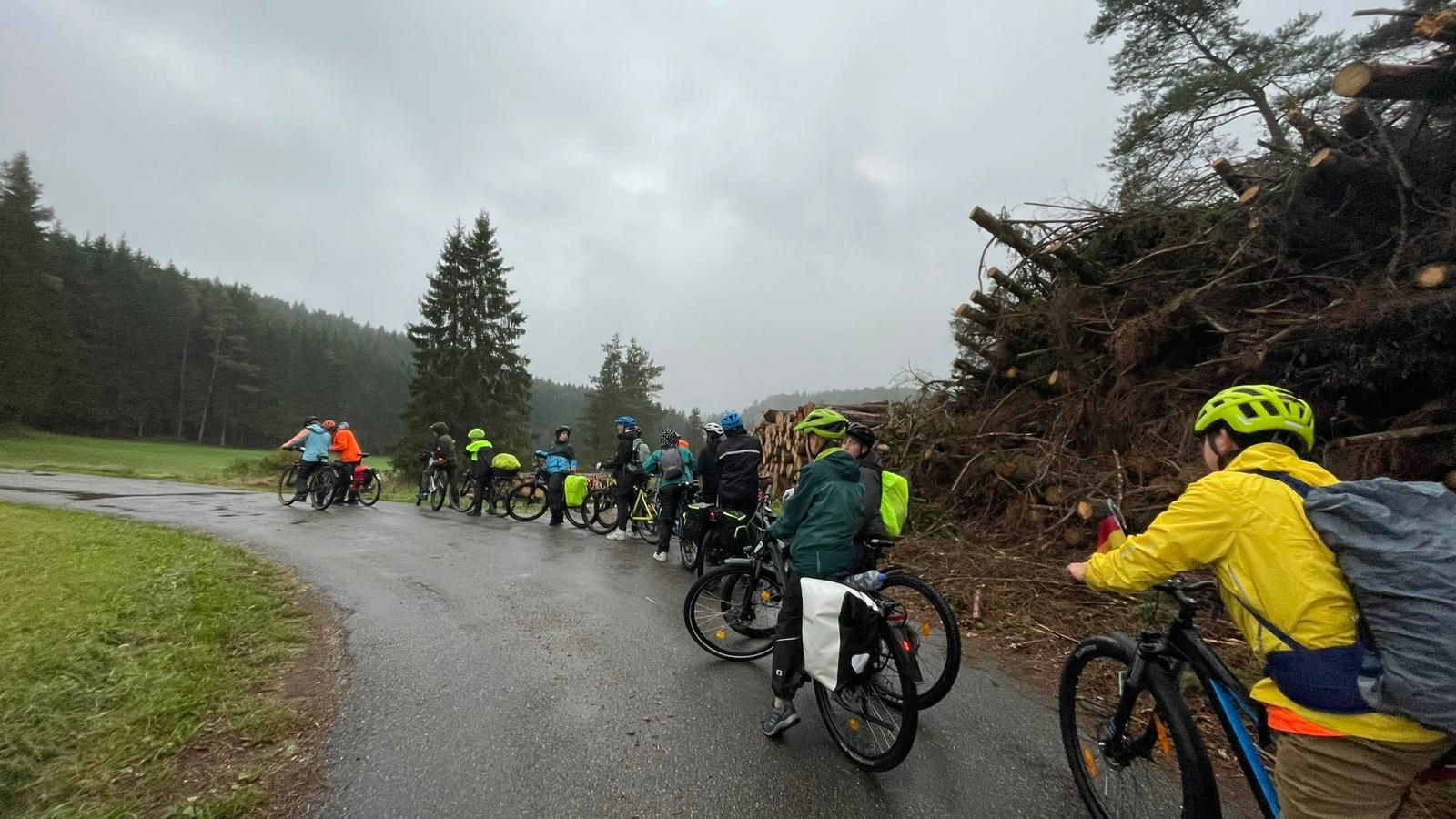 Gruppenbild, Schüler auf Fahrrädern machen halt, im Hintergrund ein Holzhaufen