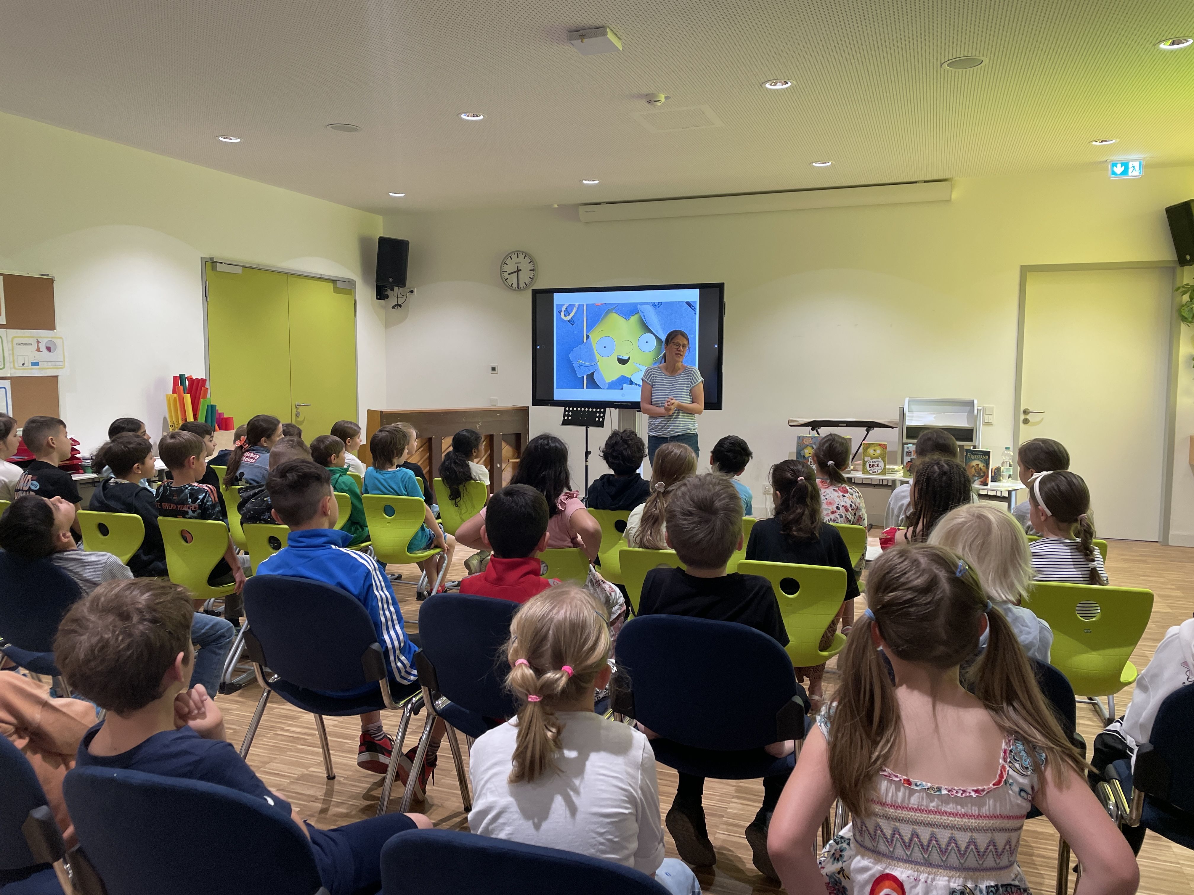 Die Autorin steht vor einer Tafel und spricht zu den Kindern.