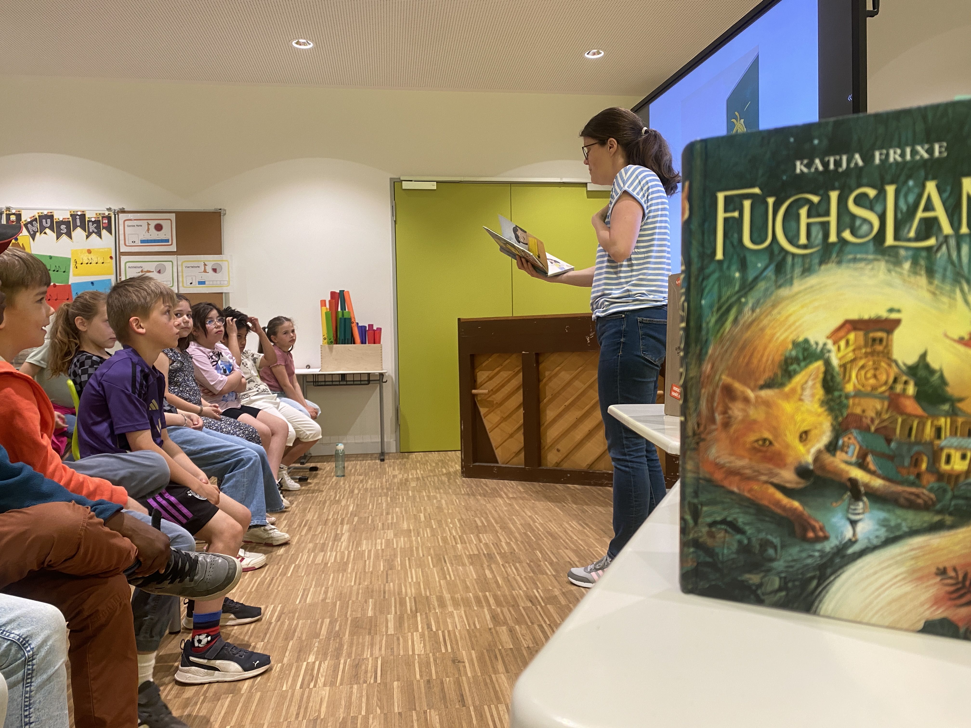 Kinder hören der Autorin zu. Im Vordergrund ist eines ihrer Bücher zu sehen.