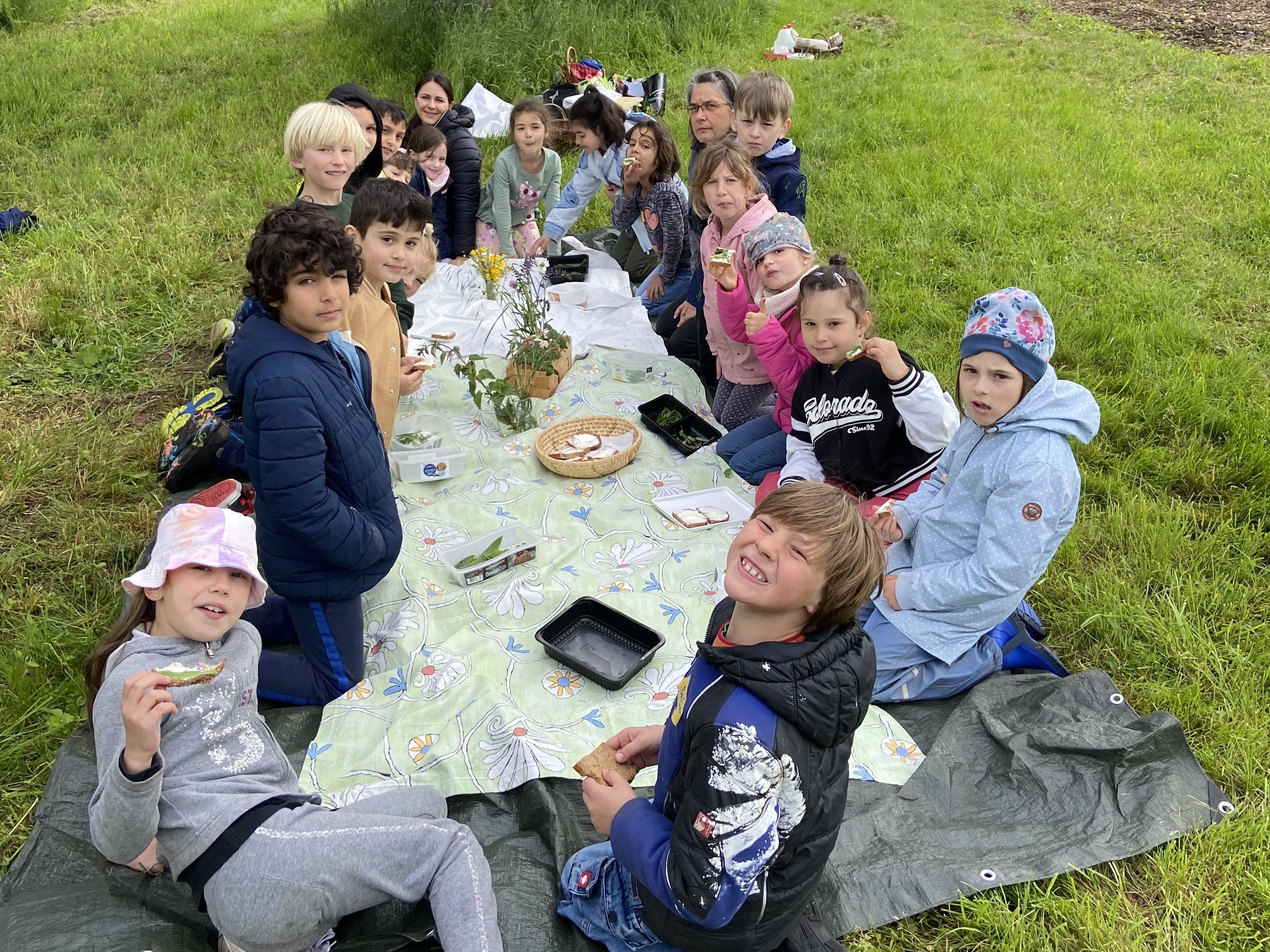 Bildbeschreibung: Kinder sitzen um eine Picknickdecke und probieren Kräuter.